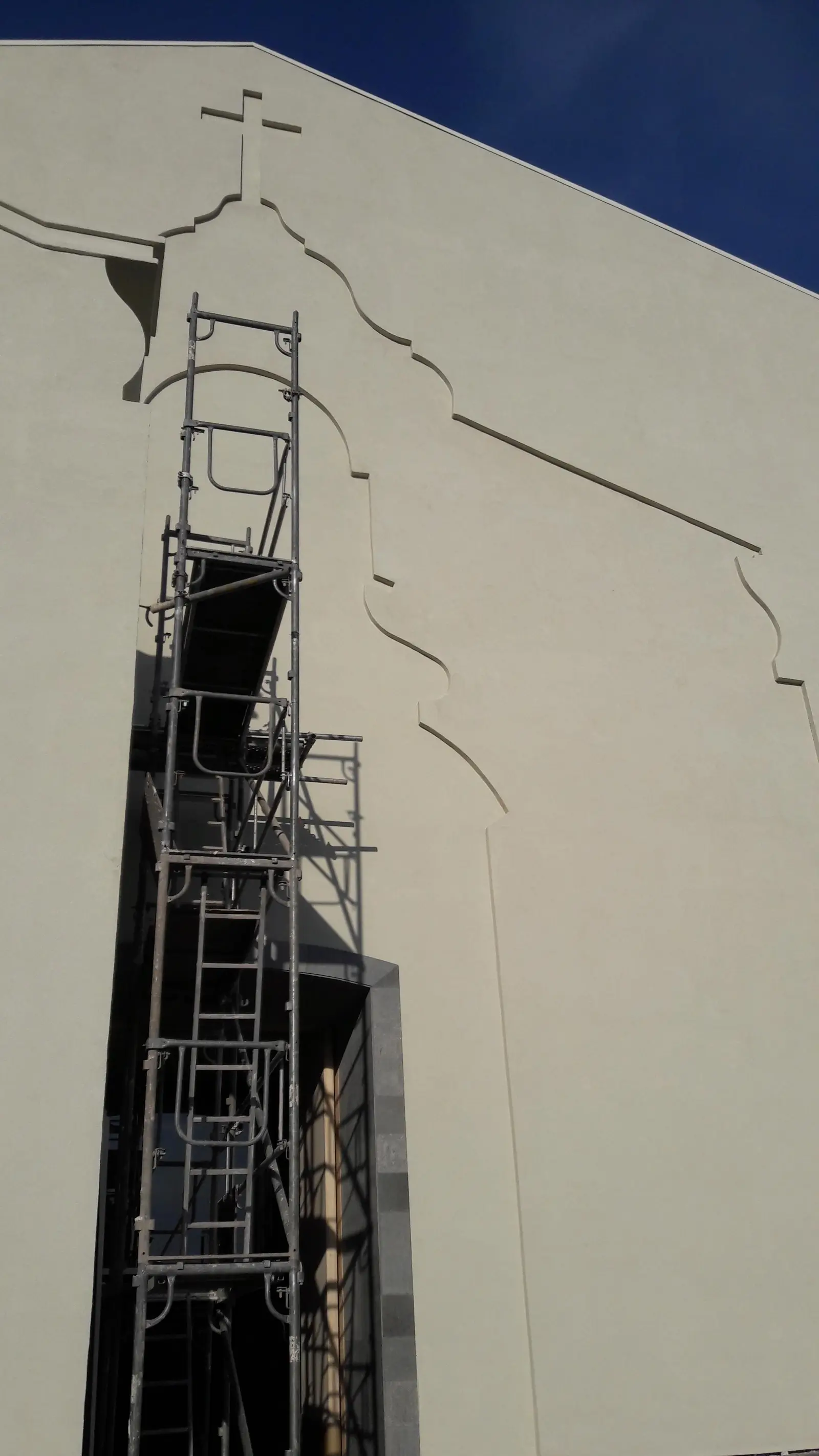 Remate de fachada de capilla con cruz durante la restauración